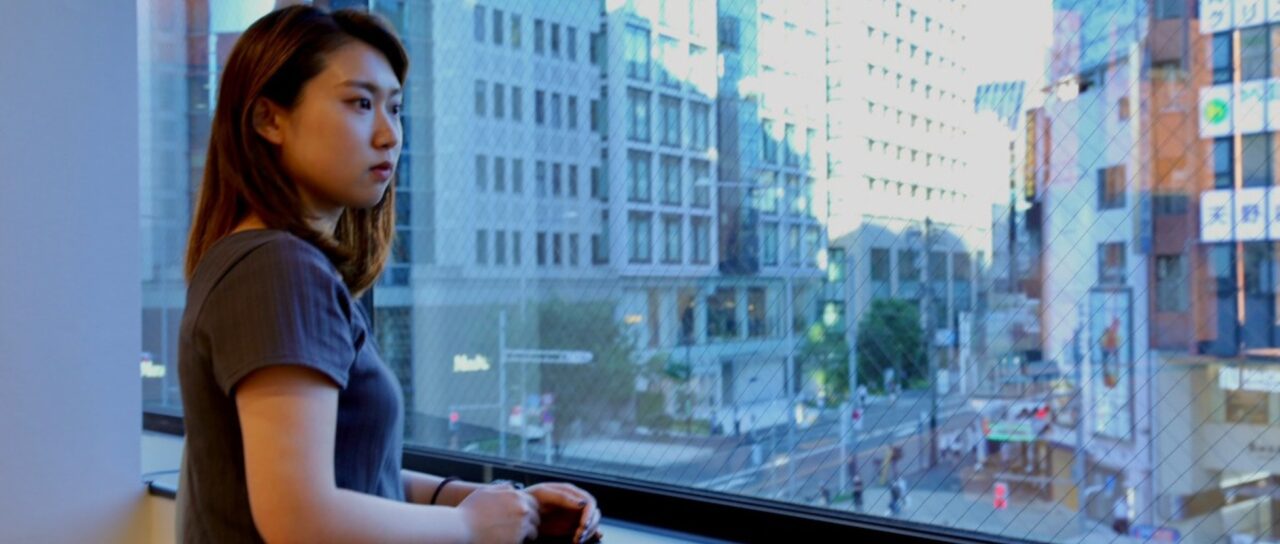 株式会社IMKのオフィスで窓の外を見つめる女性社員